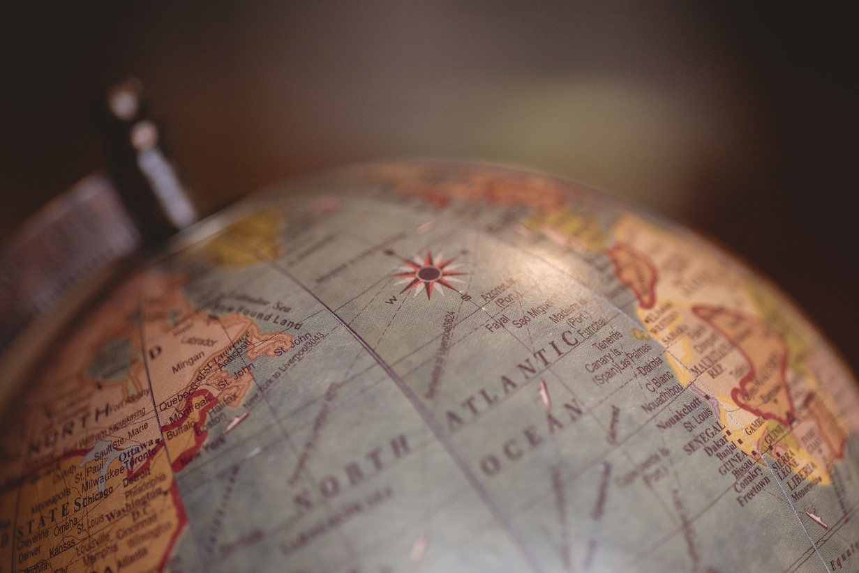 Close-up of a vintage globe showing the North Atlantic Ocean and eastern Canada, with a compass rose in focus and the rest softly blurred.